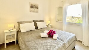 A neatly arranged bedroom with a bed, bedside tables, a wall-mounted air conditioner, and a window with curtains. - Boutique Villa Elea with private pool (Acharavi)