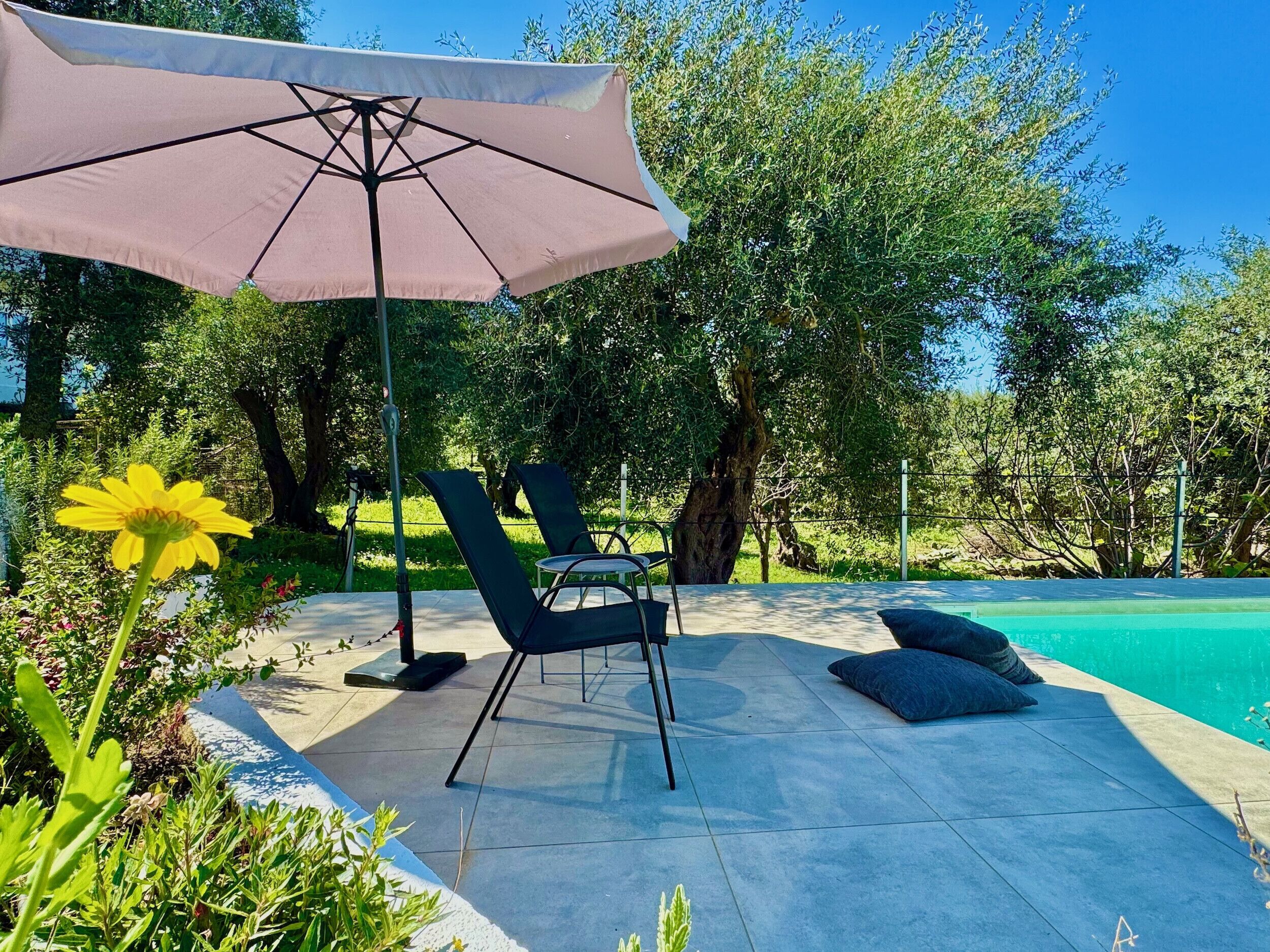 Ein Sitzbereich im Freien mit Tisch und Stühlen, einem großen Sonnenschirm und einem Pool.