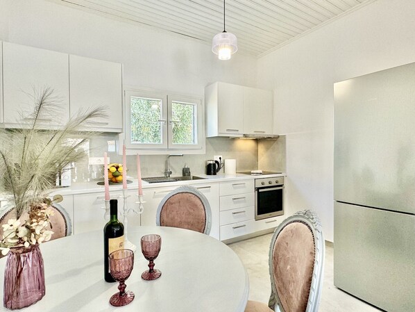 A modern kitchen with white cabinets, a stainless steel refrigerator, a dining table with chairs, and a vase with flowers.