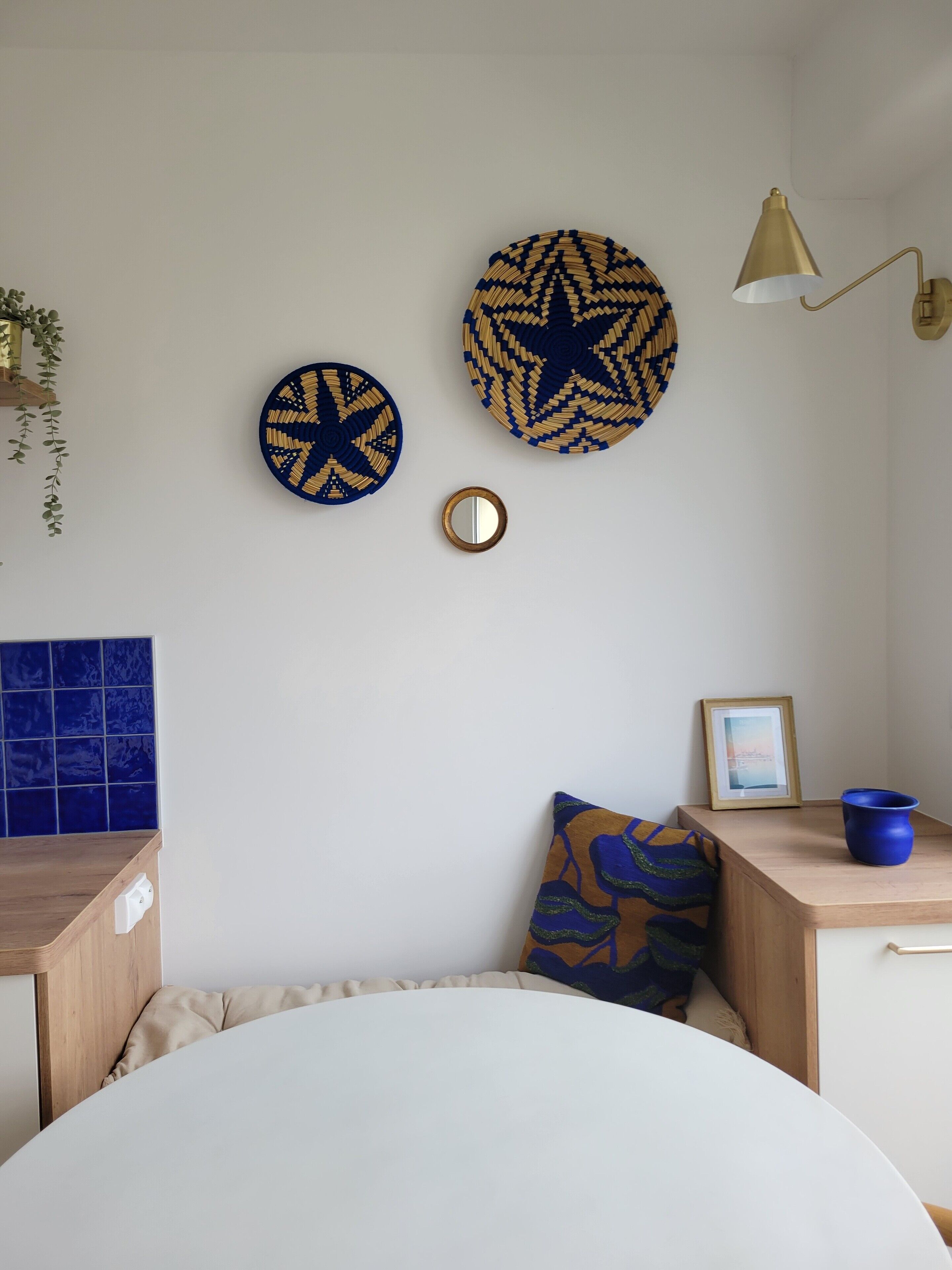 Et værelse med en rund seng, et lille bord med en blå vase, og vægdekorationer bestående af to cirkelformede motiver og et spejl.