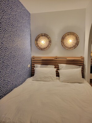 Une chambre avec un mur à motifs, une tête de lit en bois et deux lampes fixées au mur.