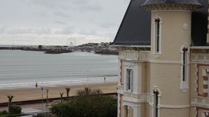 Un edificio costero con una torre, una playa y una noria al fondo.