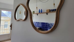 Un baño con dos espejos, un estante con artículos de aseo personal y vistas al exterior.