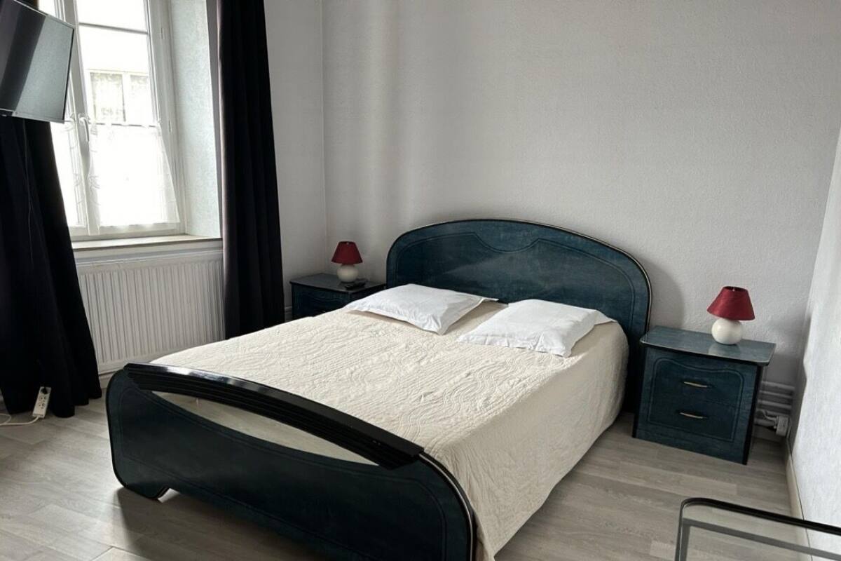 Een slaapkamer met een bed, twee nachtkastjes, een raam met gordijnen, en een lamp op elk nachtkastje.