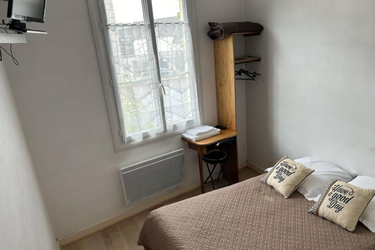 Een slaapkamer met een bed, kussens, een bureau en een stoel.