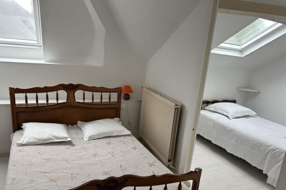 Een slaapkamer met een groot bed, een kleiner bed, een radiator en een raam.