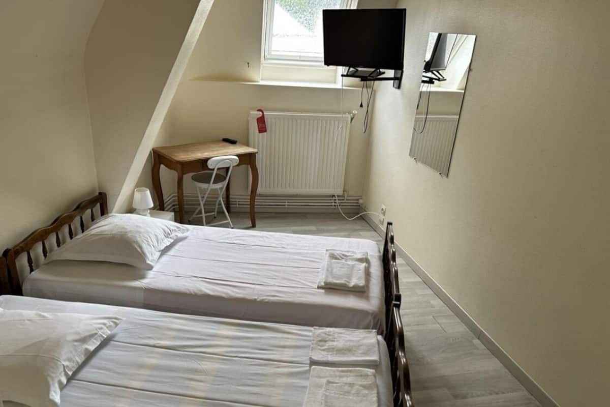 Een kleine hotelkamer met eenpersoonsbed, een bureau, een stoel, een televisie en een raam.