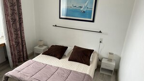 Une chambre à coucher avec un lit, deux oreillers, une table de chevet, une lampe, un tableau au mur et un rideau.