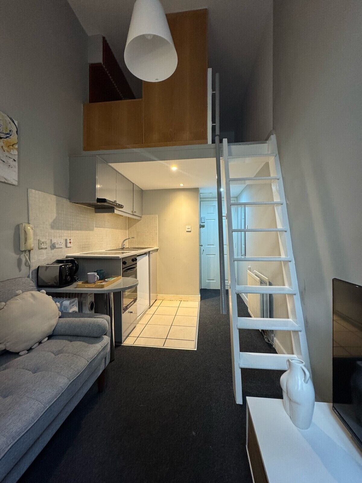 A compact living space with a kitchenette, a sofa, a TV, and a white vase.