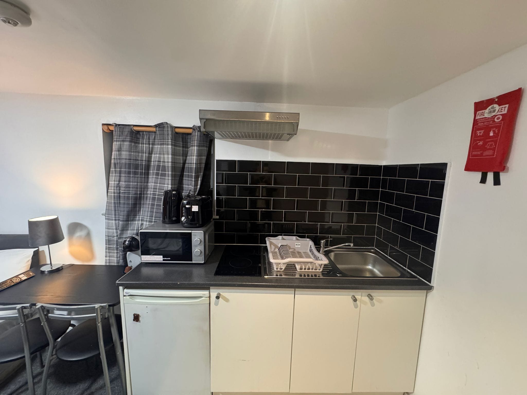 A compact kitchenette with a microwave, toaster, and coffee maker on the countertop, a sink, and a fire extinguisher on the wall.