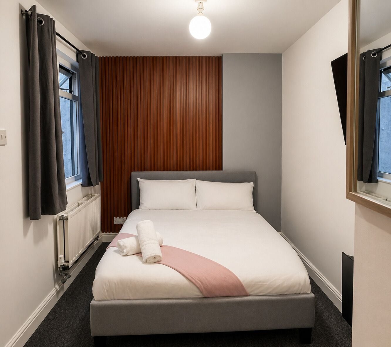 A bedroom with a bed, a radiator, a window with curtains, and a mirror.
