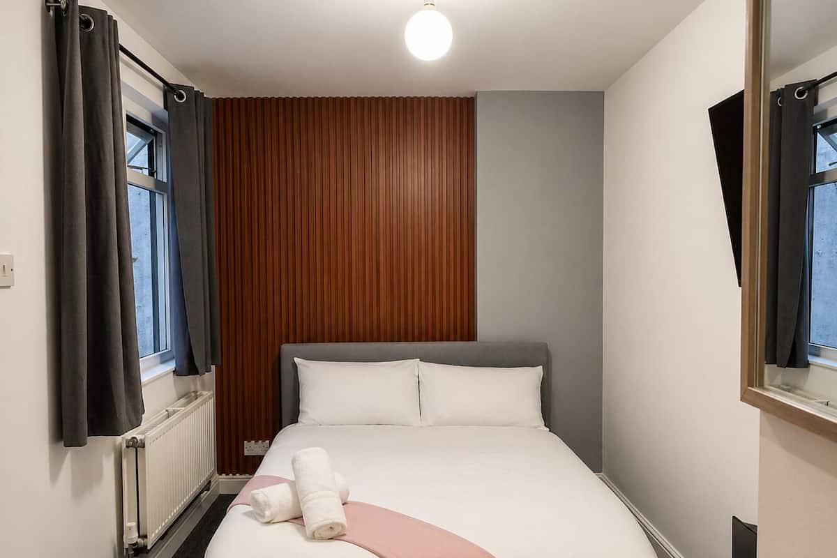 A bedroom with a bed, a radiator, a window with curtains, and a mirror.