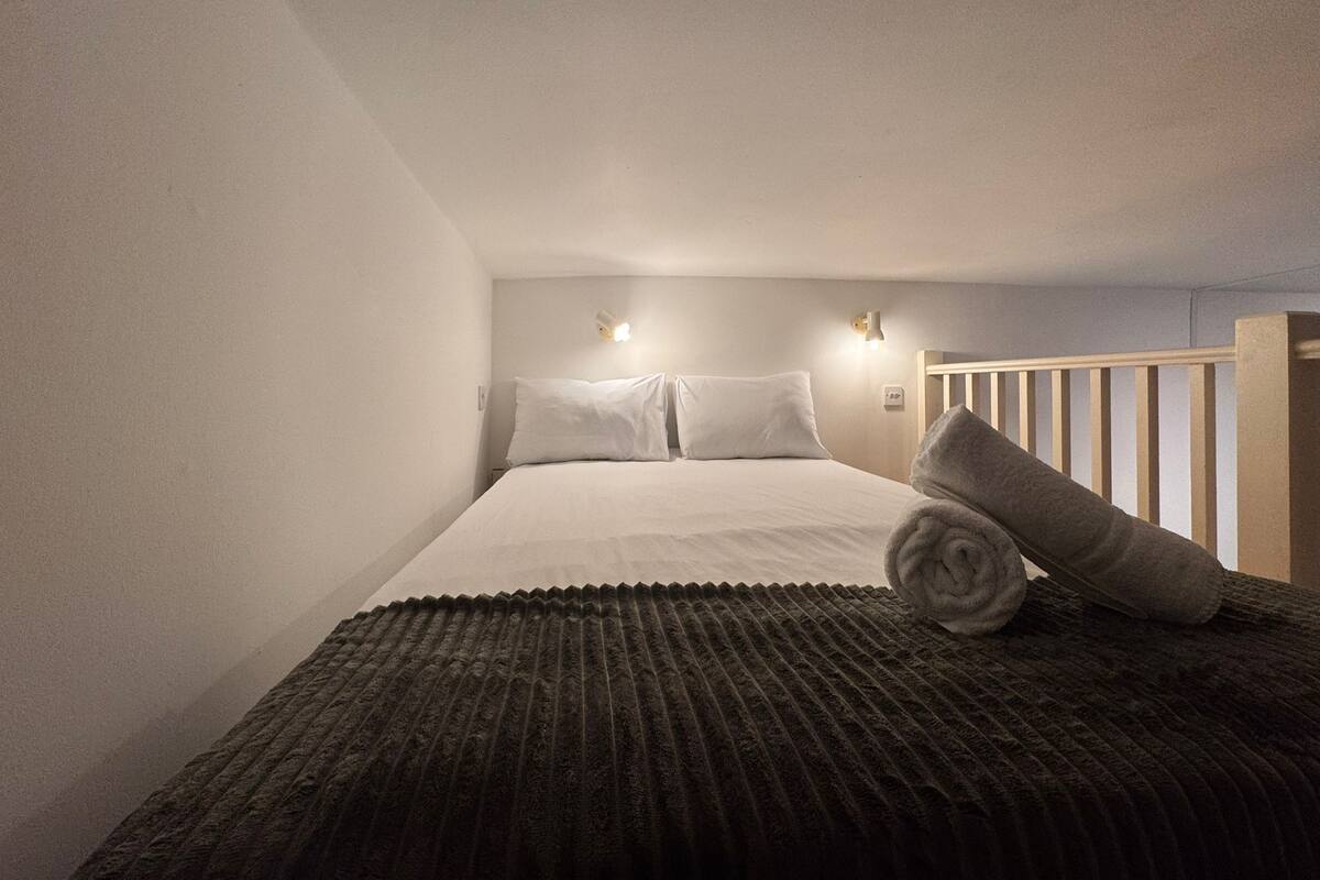A small, cozy bedroom with a single bed, a nightstand, and a wall-mounted light fixture.