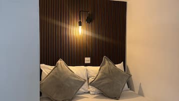 A hotel room with a bed, two pillows, a bedside lamp, and a yellow pillow on the floor.