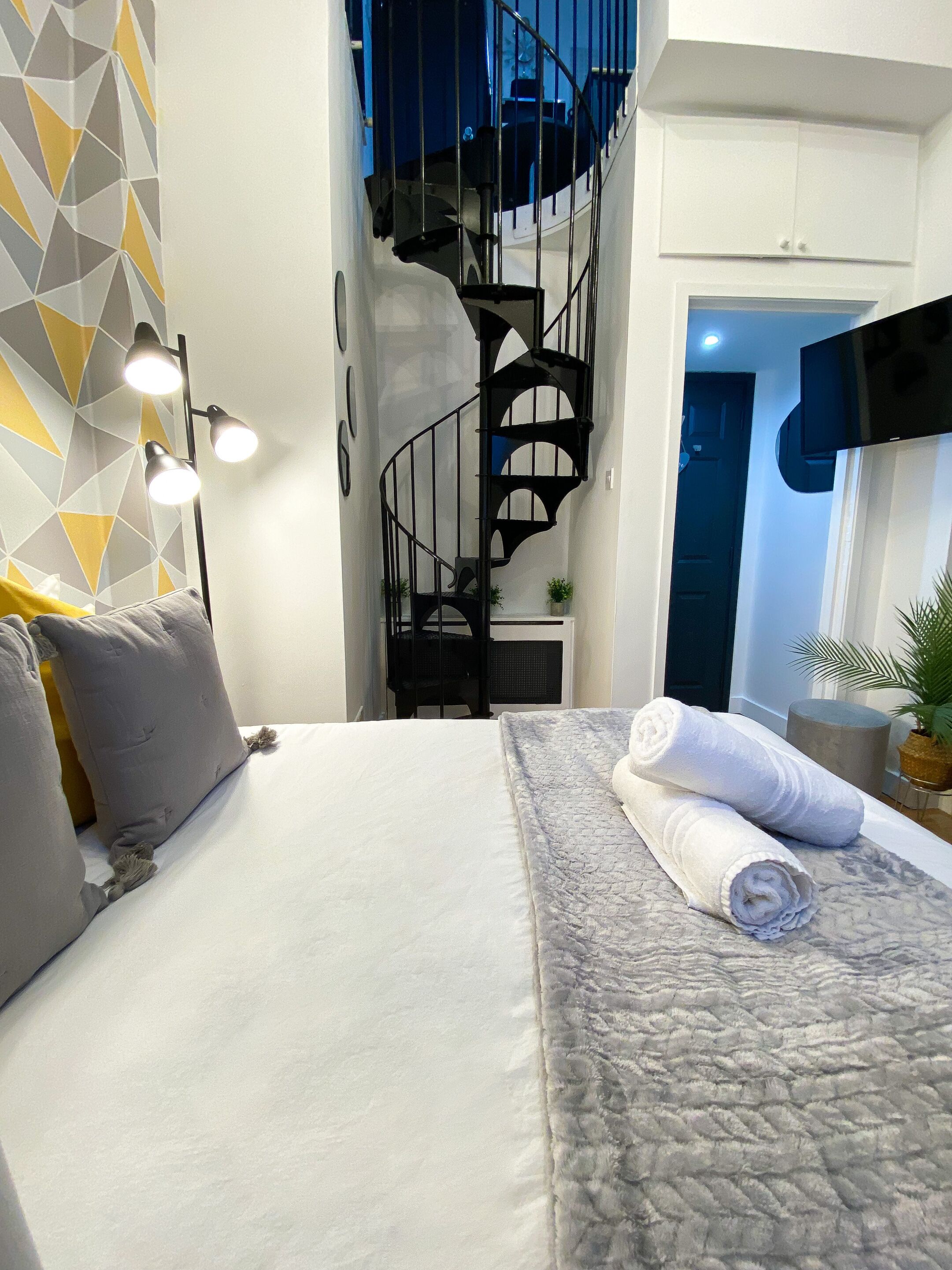 A bedroom with a bed, a wall-mounted TV, a staircase, and a geometric-patterned wall.
