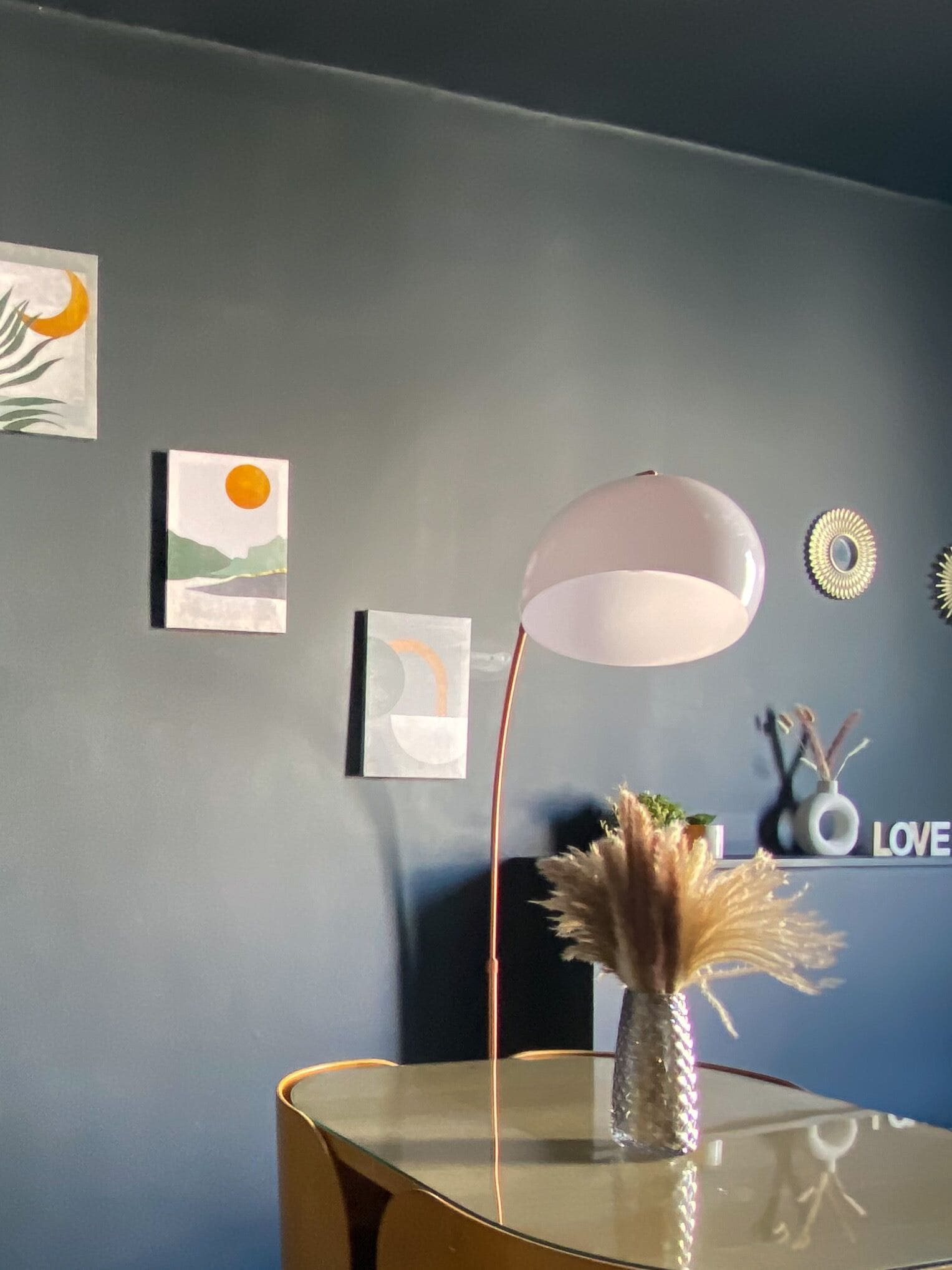 Um interior moderno com uma mesa de vidro, um vaso decorativo e obras de arte nas paredes, incluindo um sol e uma lua.