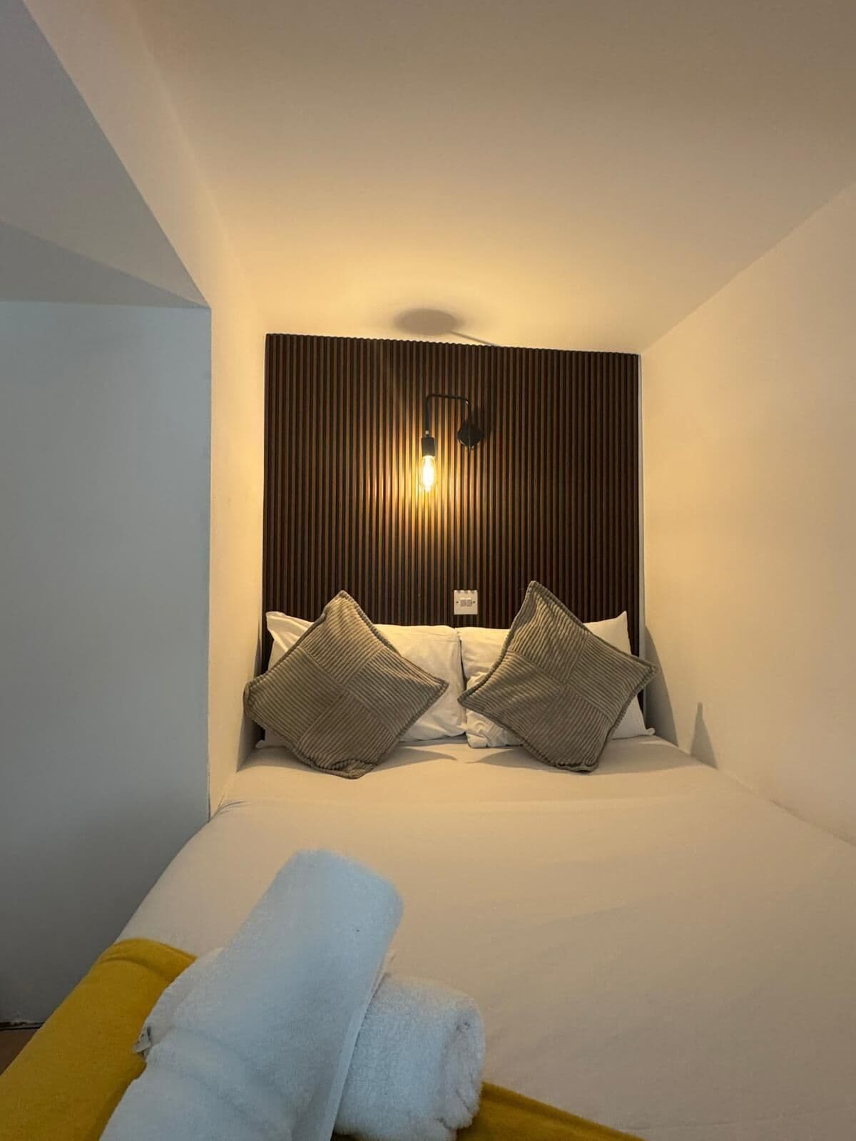 A hotel room with a bed, pillows, a headboard, and a bedside table with a towel.