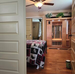 Une chambre avec un plancher en bois, un lit recouvert d’une courtepointe, un ventilateur de plafond et une armoire en bois.