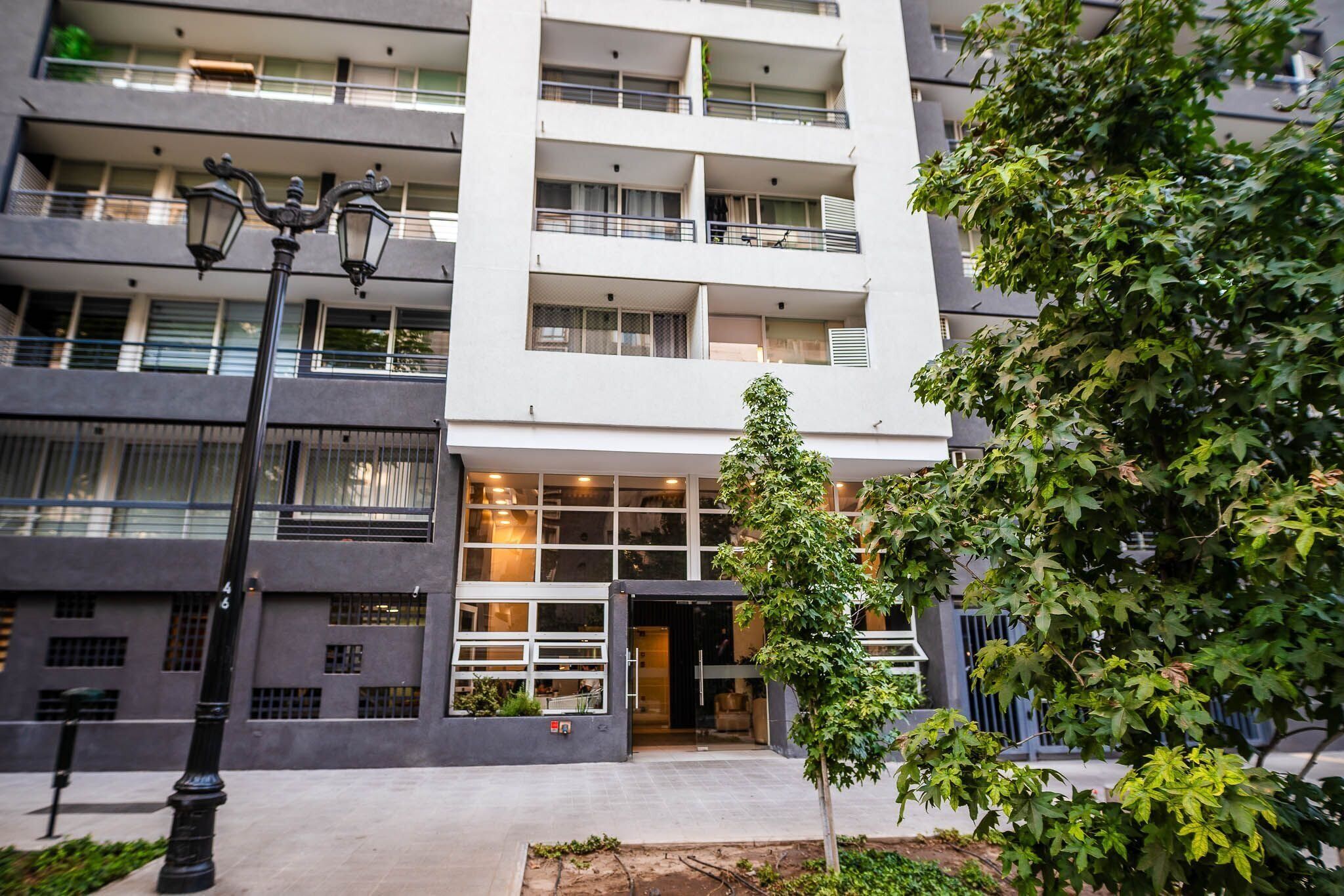 A modern multi-story building with balconies, a central entrance, and a street lamp.