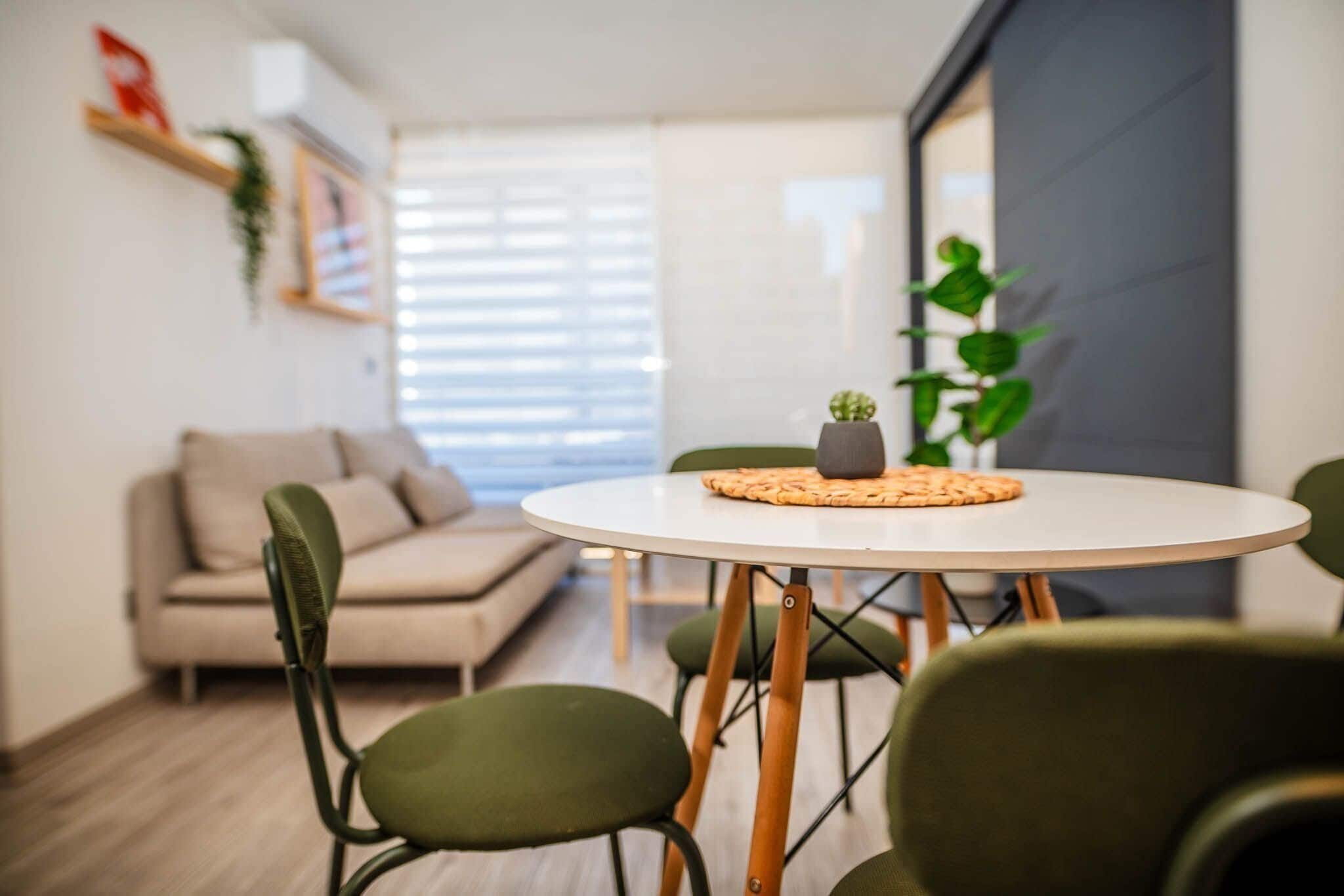 Een moderne woonkamer met een ronde tafel, groene stoelen, een bank en een potplant.
