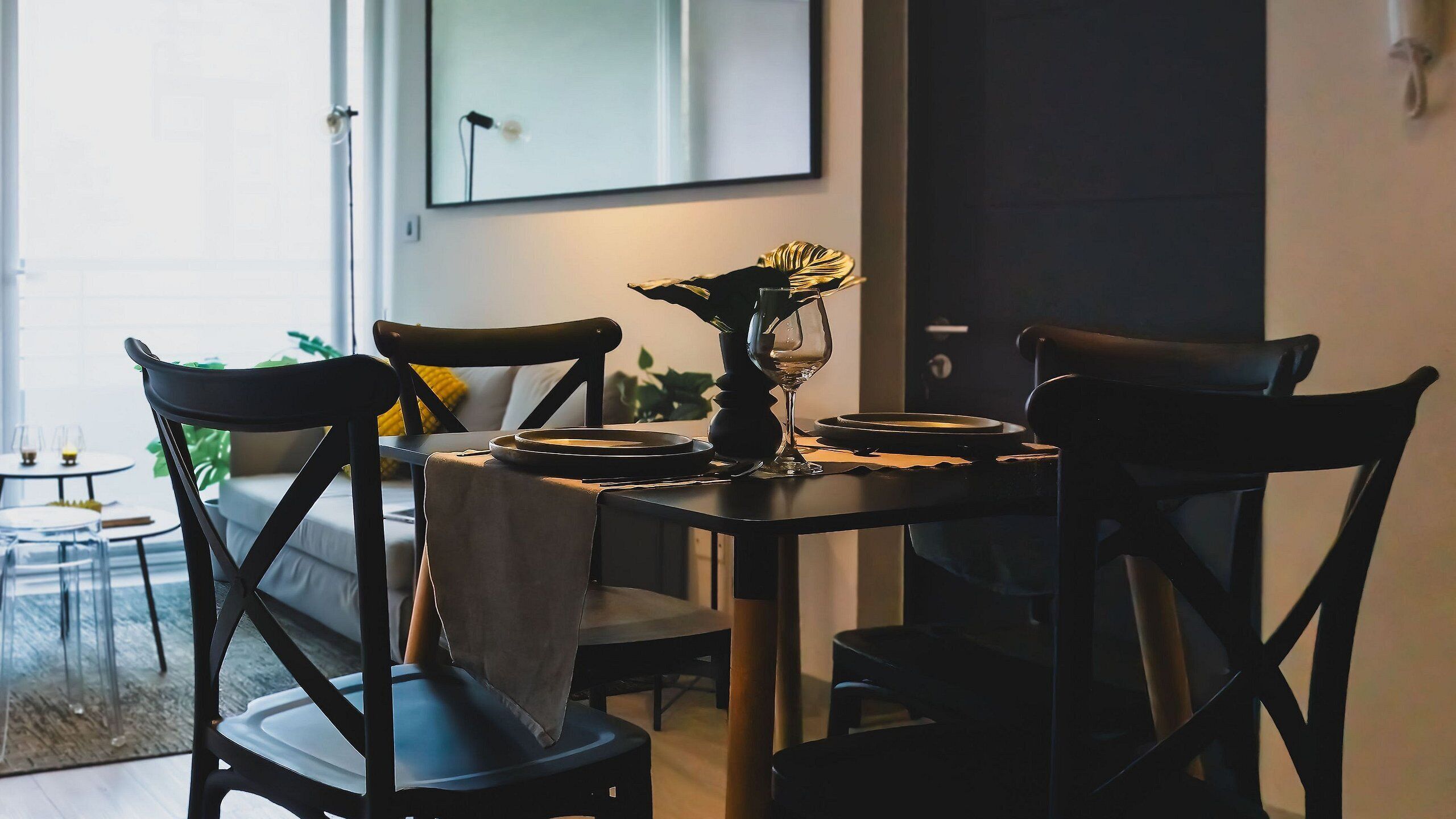 Un comedor con una mesa redonda, sillas negras y un jarrón con flores. Se observa un cuadro en la pared y una puerta al fondo.