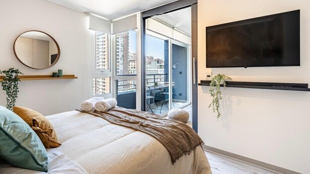 Una camera da letto moderna con un letto grande, una TV a parete e un balcone con vista su edifici alti.