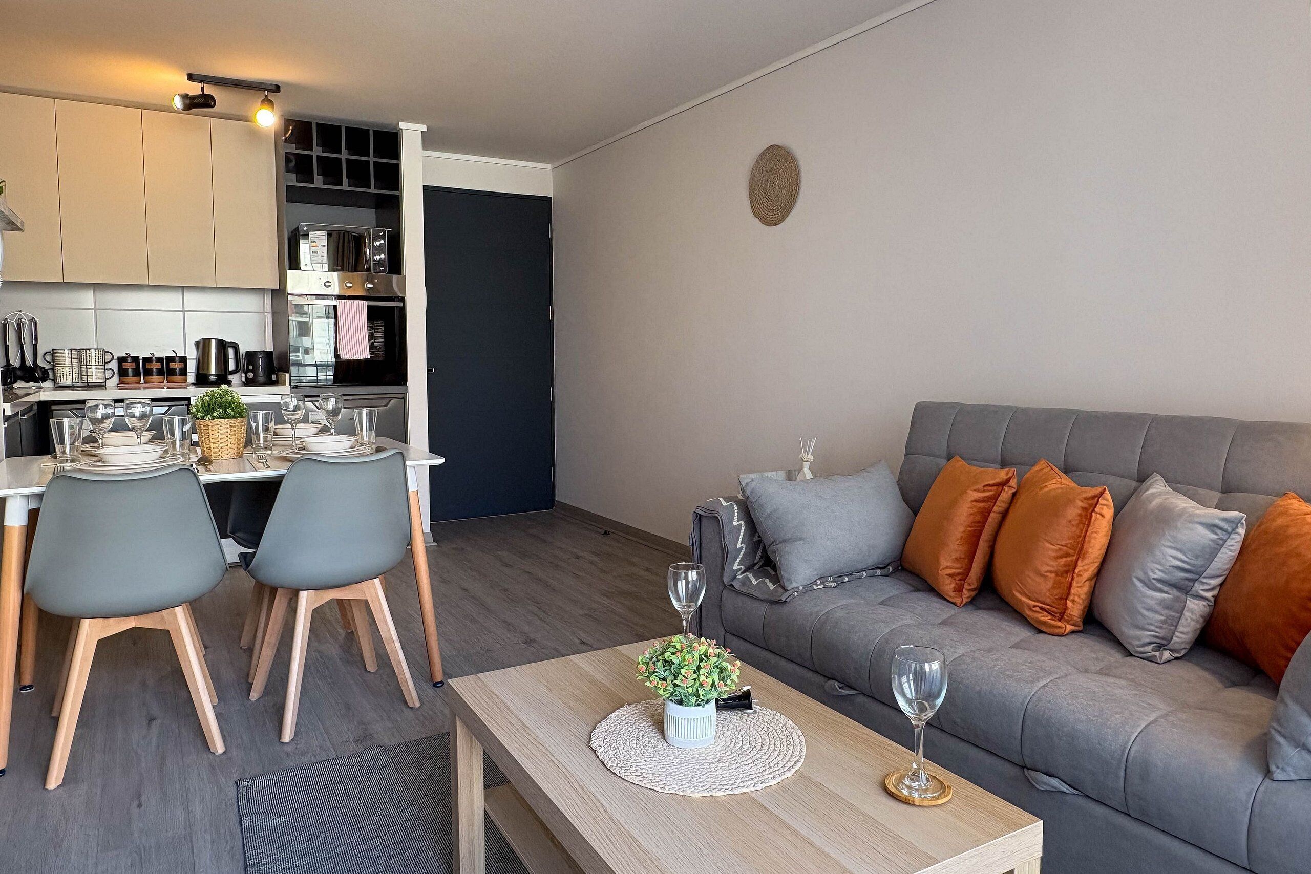Una sala de estar moderna con un sofá gris, una mesa de centro de madera y un comedor con una mesa preparada para cuatro personas.