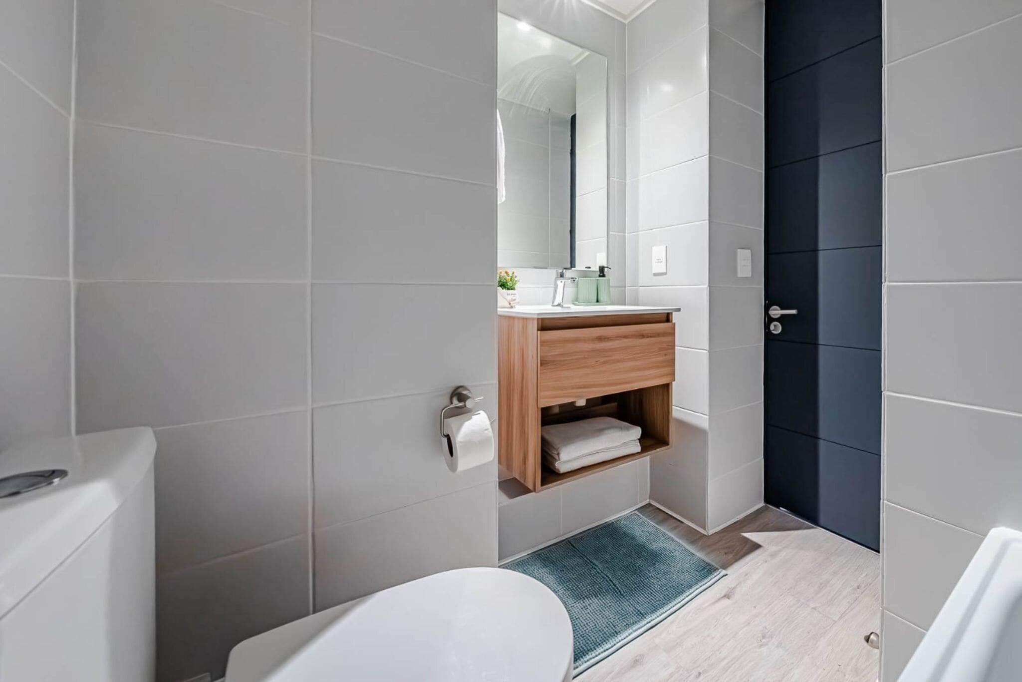 A modern bathroom with a white toilet, a wooden vanity, a mirror, and a dark door.