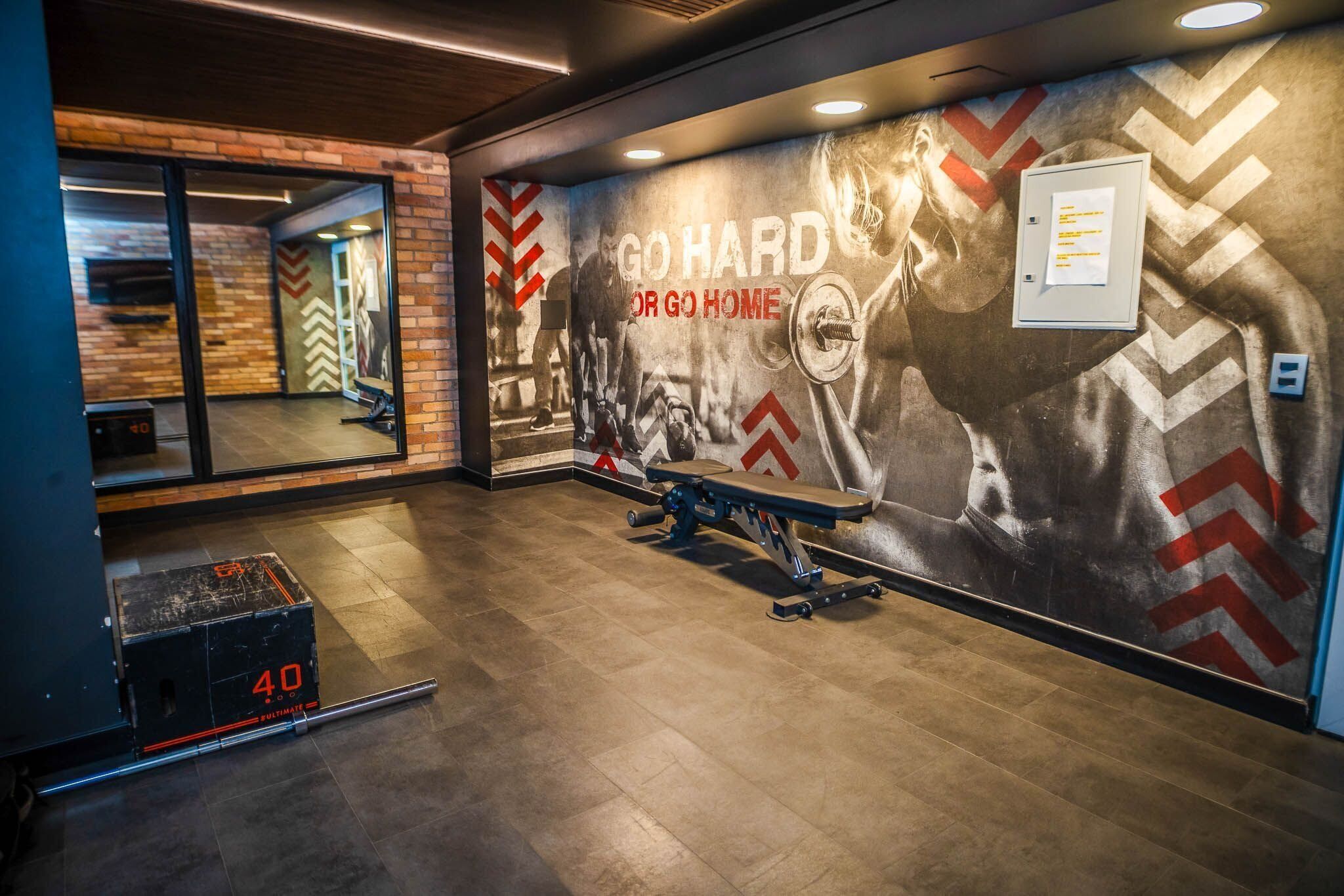 A gym with a motivational mural, a bench press, and a weight rack.
