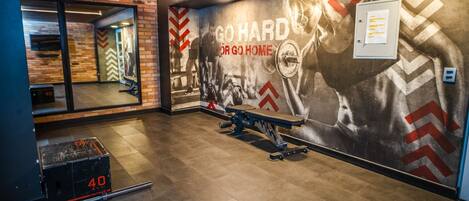A gym with a motivational mural, a bench press, and a weight rack.