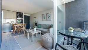 Un appartamento moderno con zona pranzo, angolo cottura, soggiorno e un balcone con tavolo e sedie in vetro.