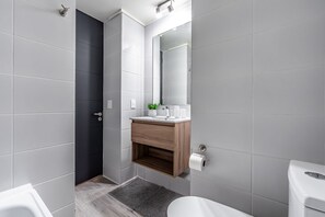 Un baño moderno con azulejos grises, un mueble de tocador de madera, un espejo y un inodoro.