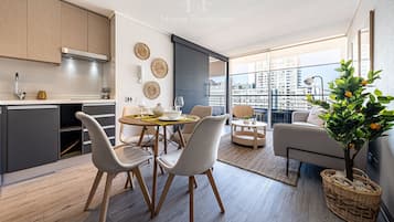 Una cocina moderna con comedor, un balcón con vistas a la ciudad y una sala de estar con sofá y planta.