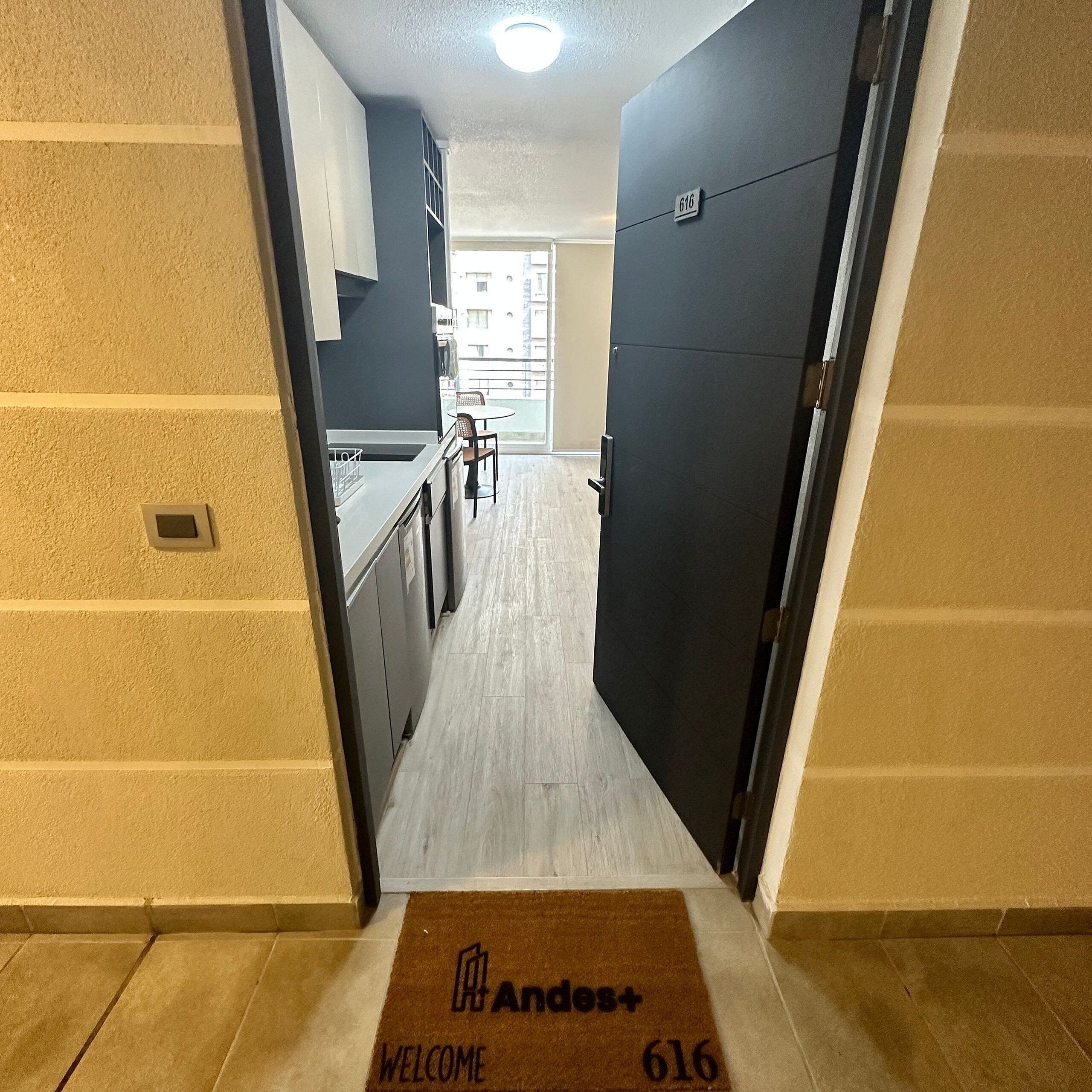 A narrow hallway with a doormat reading "Andes+ Welcome 616" leading to a kitchen area with cabinets and a dining table.