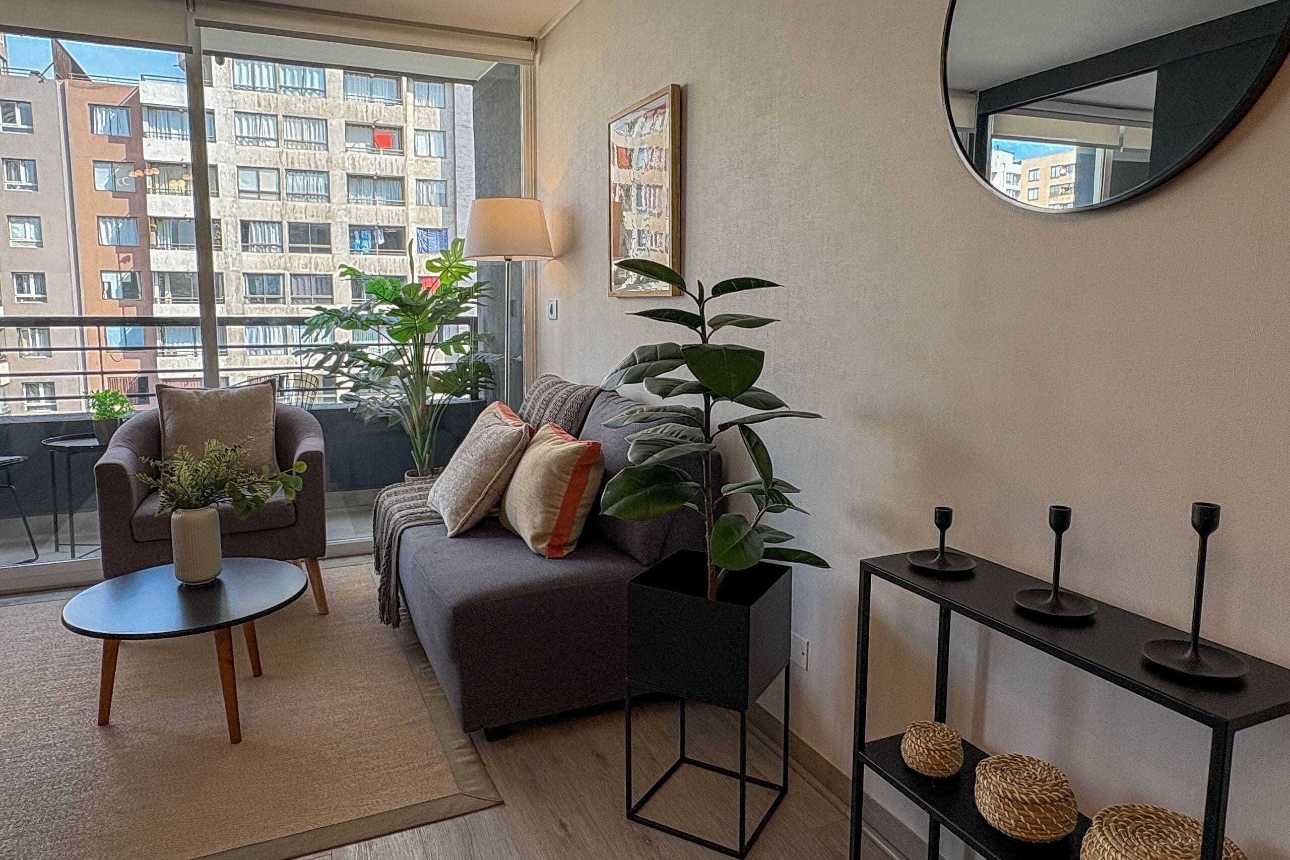 Een moderne woonkamer met een grijze bank, een ronde salontafel en een zwart bijzettafeltje met decoratieve objecten.