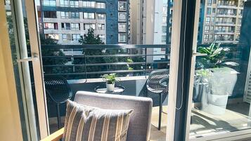 Un balcón con vistas a edificios altos, una mesa pequeña con una planta en maceta y dos sillas.
