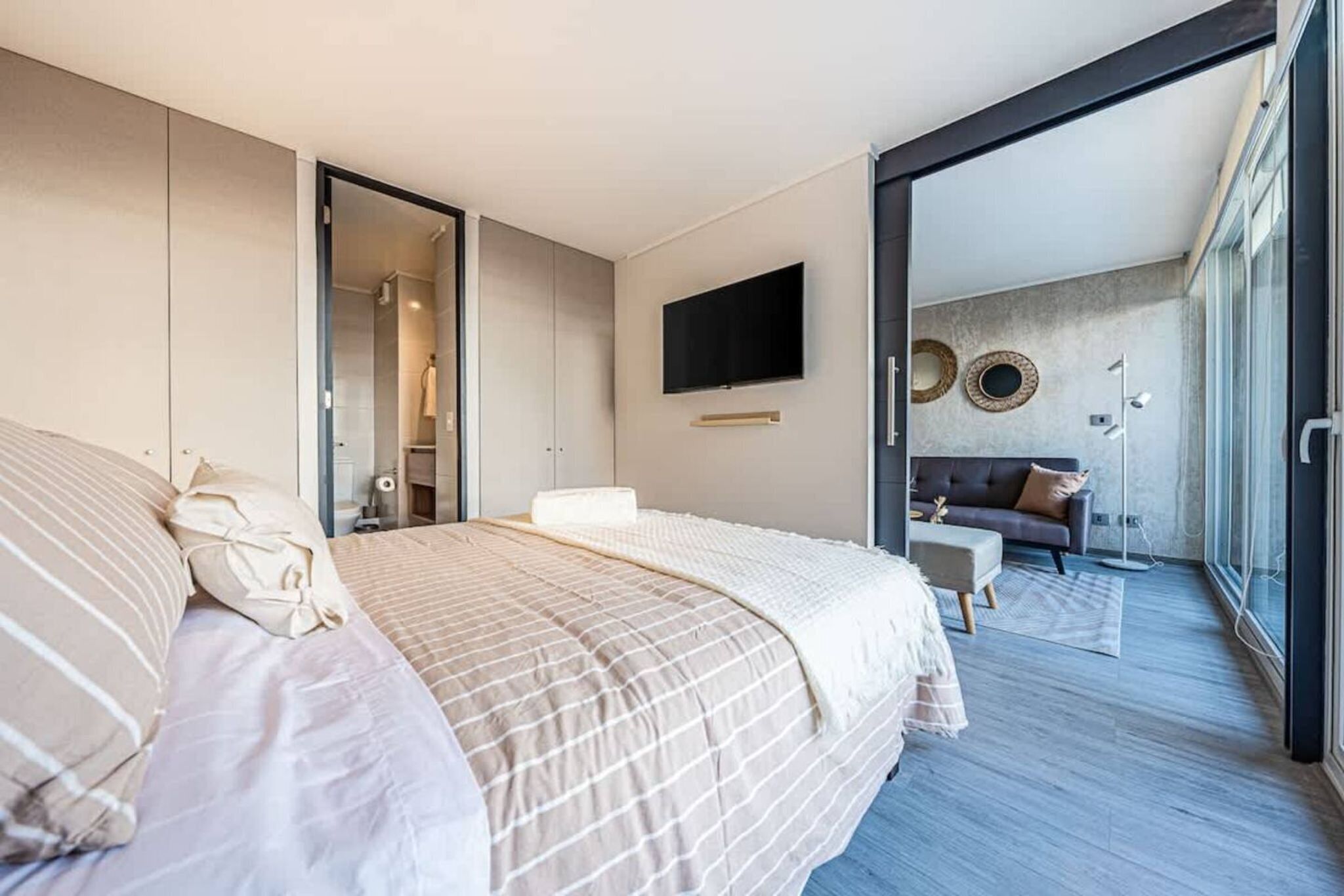 Une chambre moderne avec un grand lit, un téléviseur fixé au mur et un canapé dans le salon attenant.