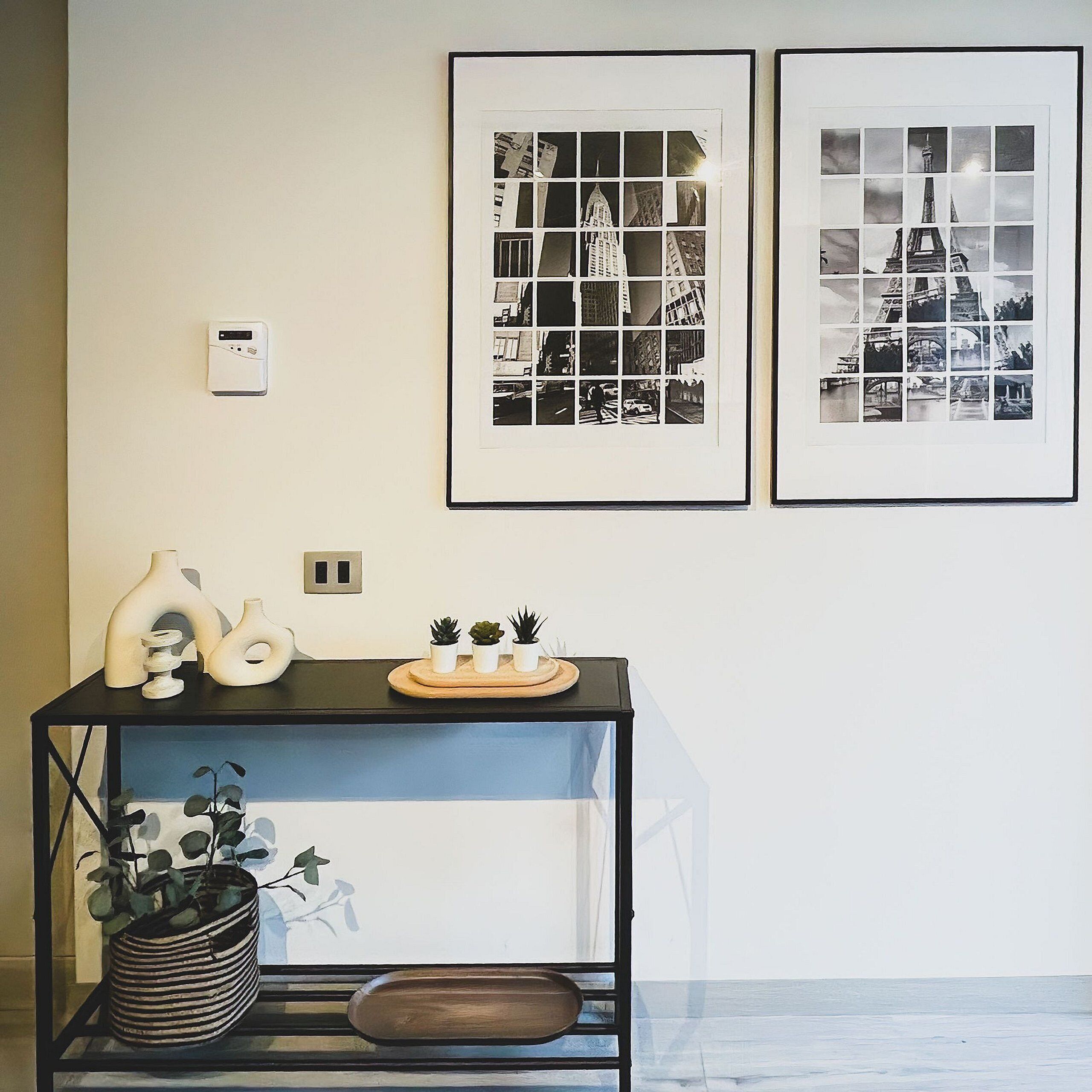 A room with a black metal shelf holding decorative items and a framed collage of cityscape photos on the wall.