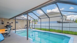 A covered outdoor swimming pool with a patio area, a grill, and a view of neighboring houses. - Disney Castle Cove - Private Pool & Community Boat Ramp close to Legoland (Winter Haven)