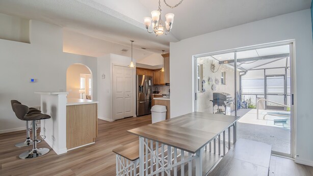 A modern kitchen with a central island, a dining area with a bench, and a view of the outdoors through a glass door. - Disney Castle Cove - Private Pool & Community Boat Ramp close to Legoland (Winter Haven)