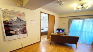 A hotel room with a wooden floor, a TV on a stand, a poster of Tokyo, and a door leading to another room. - 1minute walk to station, direct bus to Haneda Airport! Easy access! (大田区)