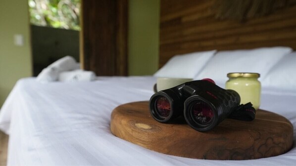 A bed with white linens, a wooden headboard, and a pair of binoculars on a wooden block. - Montés Samaná (San Carlos)