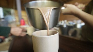 A person pouring a liquid from a metal container into a ceramic mug. - Montés Samaná (San Carlos)