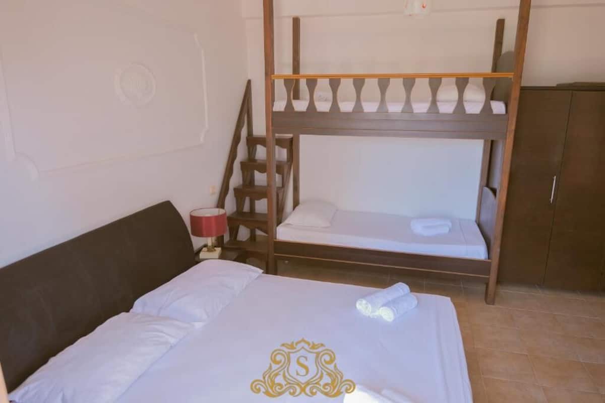 A room with a bunk bed, a single bed, a nightstand with a lamp, and a wardrobe.