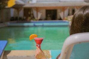 Una persona che tiene un cocktail a bordo piscina.