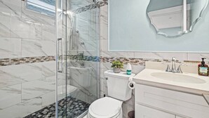 A modern bathroom with a glass-enclosed shower, a toilet, and a sink with a mirror above it. - Modern Cozy 3BR-2BA Apt Near T (Boston)