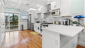 A modern kitchen with white cabinetry, a central island, stainless steel appliances, and a view to the outdoors. - Modern Cozy 3BR-2BA Apt Near T (Boston)