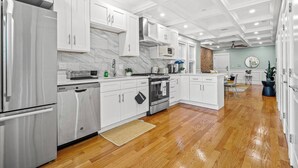A modern kitchen with white cabinetry, a stainless steel refrigerator, and a wooden floor. - Modern Cozy 3BR-2BA Apt Near T (Boston)