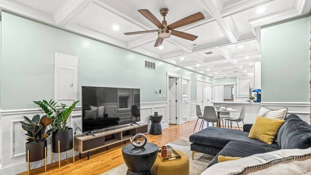A modern living room with a flat-screen TV, a ceiling fan, and a dining area in the background. - Modern Cozy 3BR-2BA Apt Near T (Boston)