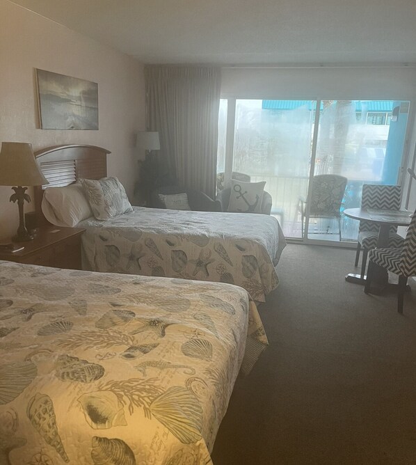 Quarto de hotel com duas camas, uma escrivaninha, uma cadeira e vista para o exterior.